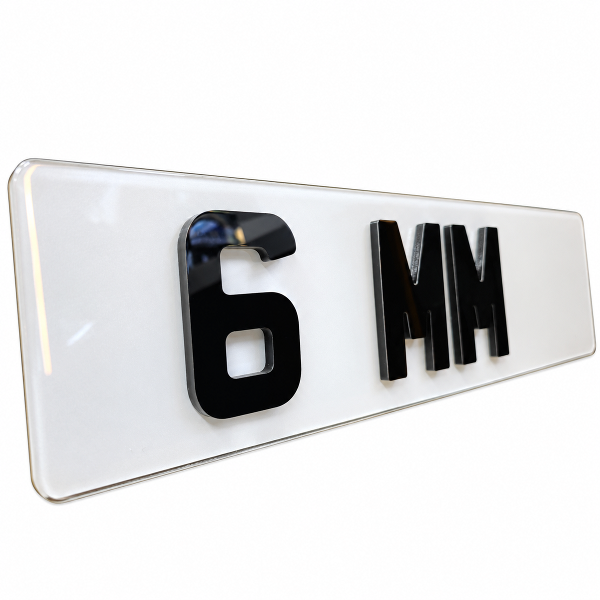 A glossy white rectangular license plate or plate-style sign with raised black characters reading '6 MM' on a clean white background.