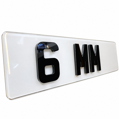 A glossy white rectangular license plate or plate-style sign with raised black characters reading '6 MM' on a clean white background.