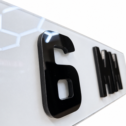 Close-up of glossy black 3D lettering on a white sign, showing the number 6 and partial letters that spell out MM.