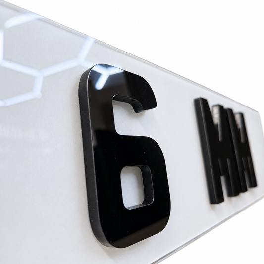 Close-up of glossy black 3D lettering on a white sign, showing the number 6 and partial letters that spell out MM.