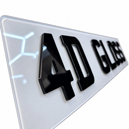 Close up of A glossy white rectangular license plate badge with raised black lettering reading '4D GLOSS' on a plain white background.